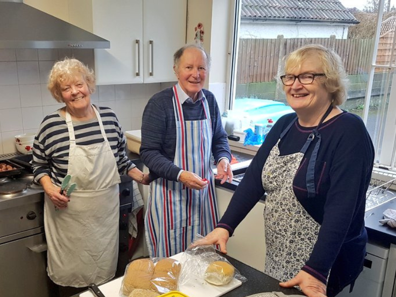 Three people volunteering in a kitchen, smiling at camera